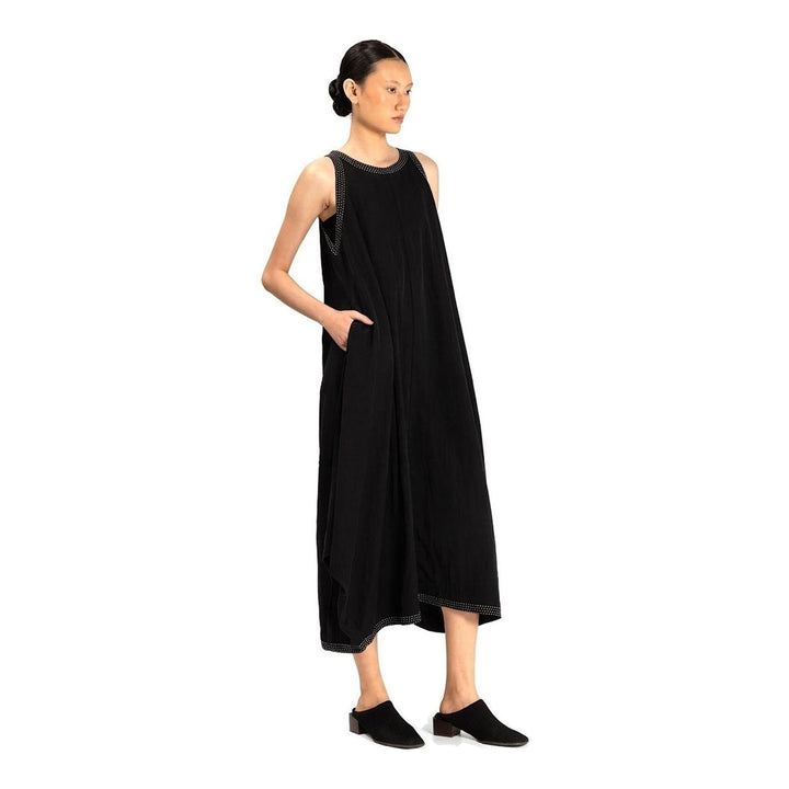 Model wearing an Anaabu black sleeveless midi dress with a voluminous A-line silhouette, asymmetric handkerchief hemline, and fine metallic stud trim at the neckline and hem - packshot