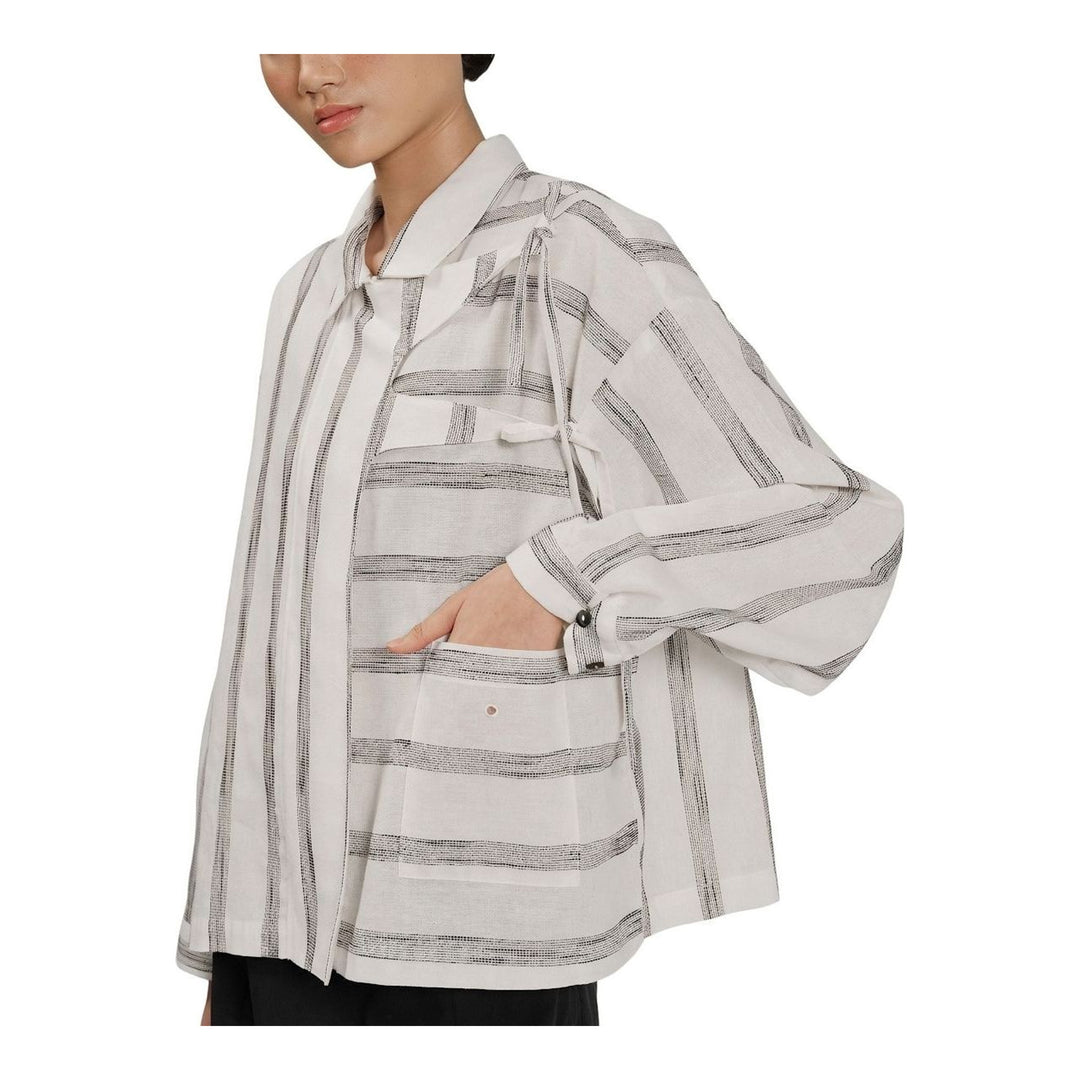 Model wearing Anaabu Asymmetrical Batwing Top in black textured fabric with an open collar, asymmetric front placket, patch chest pocket, and long batwing sleeves, styled with dark drop-crotch trousers and brown mules - packshot