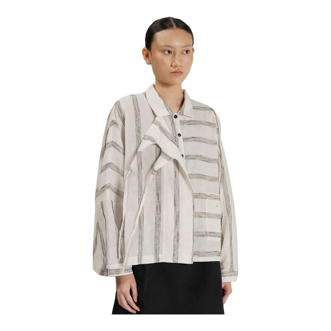 Model wearing Anaabu Asymmetrical Batwing Top in black textured fabric with an open collar, asymmetric front placket, patch chest pocket, and long batwing sleeves, styled with dark drop-crotch trousers and brown mules - packshot