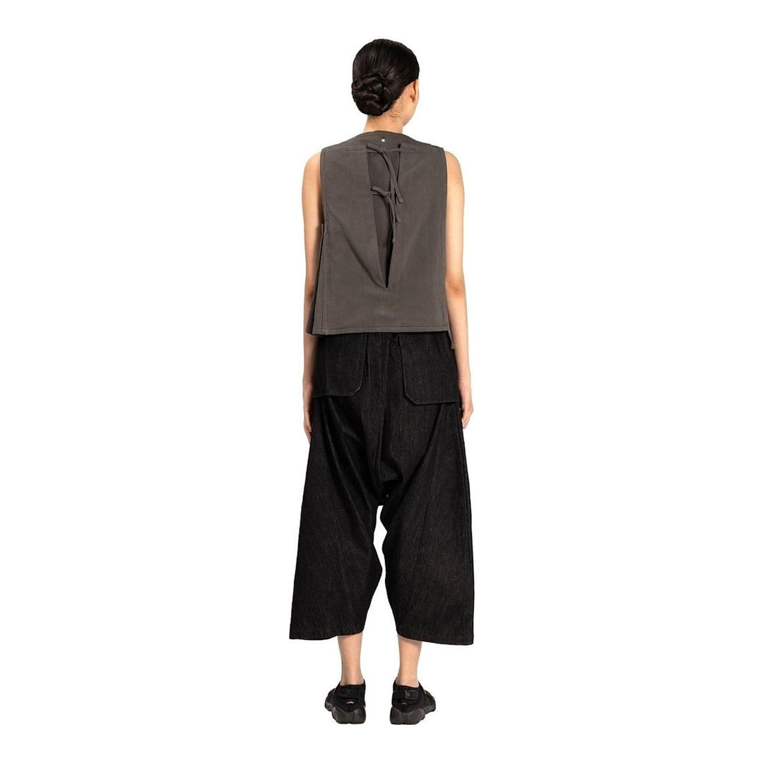Model wearing the Anaabu Asymmetrical Vest in black, featuring an asymmetric neckline, diagonal panelling, and a draped fringe tie at the shoulder, styled with wide-leg black trousers and dark leather sandals. - packshot