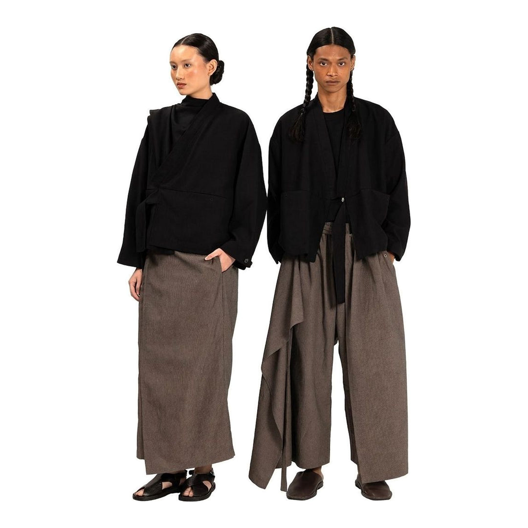 Model wearing the Anaabu Shawl Jacket in black — a draped wrap-style jacket with oversized shawl collar and self-tie belt, styled over a black turtleneck and olive wide-leg trousers - packshot