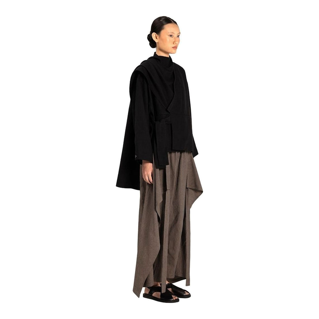 Model wearing the Anaabu Shawl Jacket in black — a draped wrap-style jacket with oversized shawl collar and self-tie belt, styled over a black turtleneck and olive wide-leg trousers - packshot