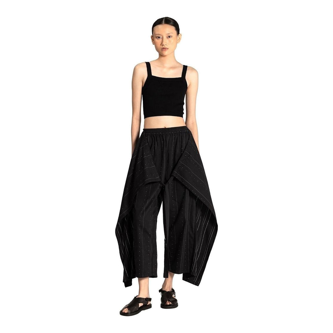 Model wearing Anaabu The Skants — black wide-leg cropped pants with large draped overlay panels featuring pinstripe and dot print, paired with a black square-neck crop top and leather sandals - packshot