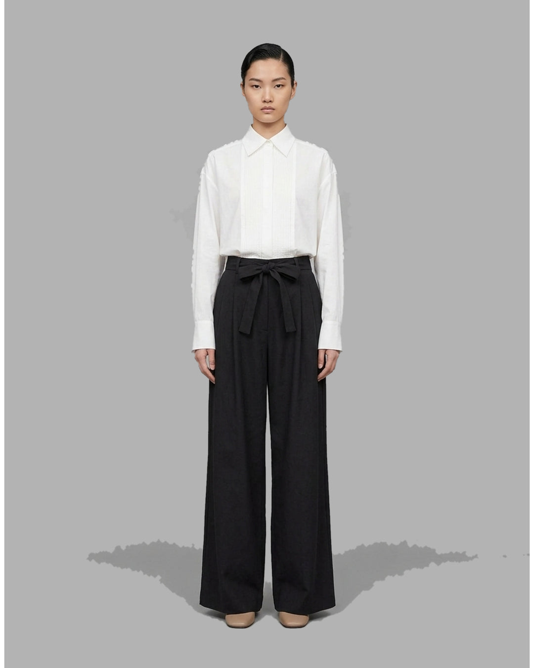 Black high-waisted wide-leg pants with front pleats and a self-tie belt at the waist, shown from the front - front