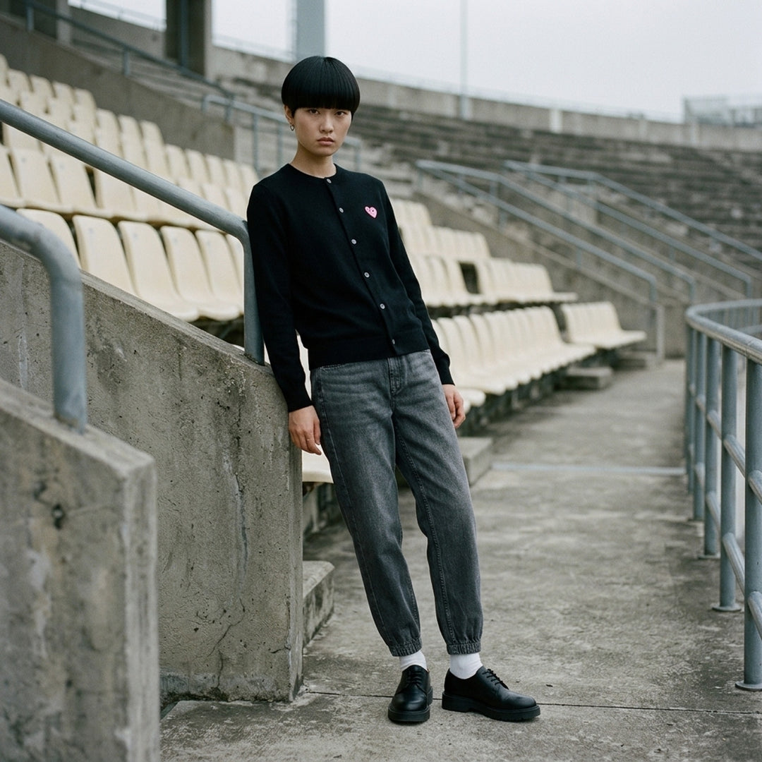 Comme des Garçons PLAY black round neck cardigan with embroidered pink heart emblem patch and button-through front fastening, flat lay view - lifestyle
