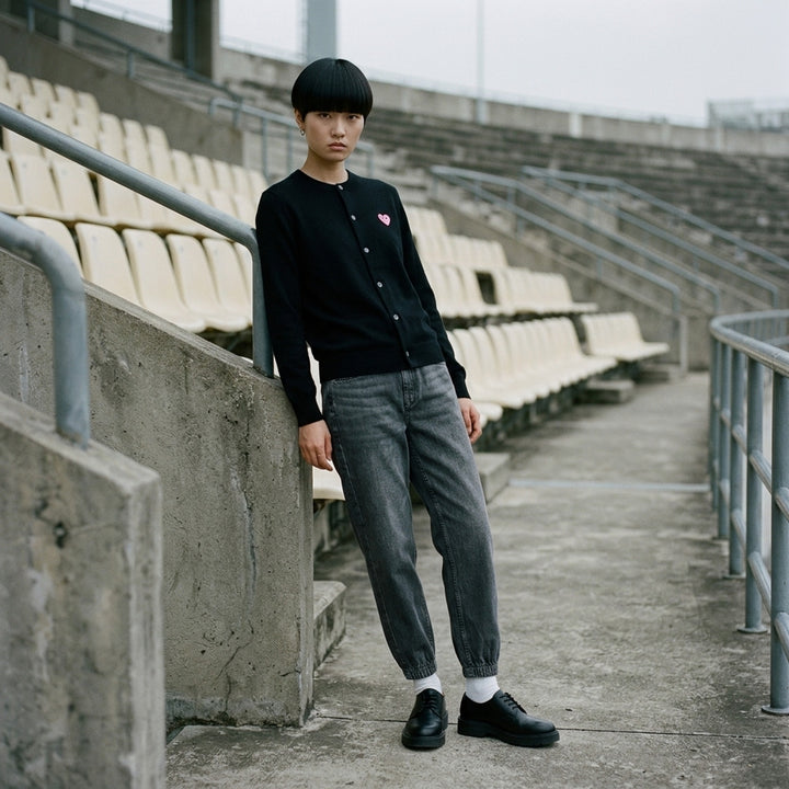 Comme des Garçons PLAY black round neck cardigan with embroidered pink heart emblem patch and button-through front fastening, flat lay view - lifestyle