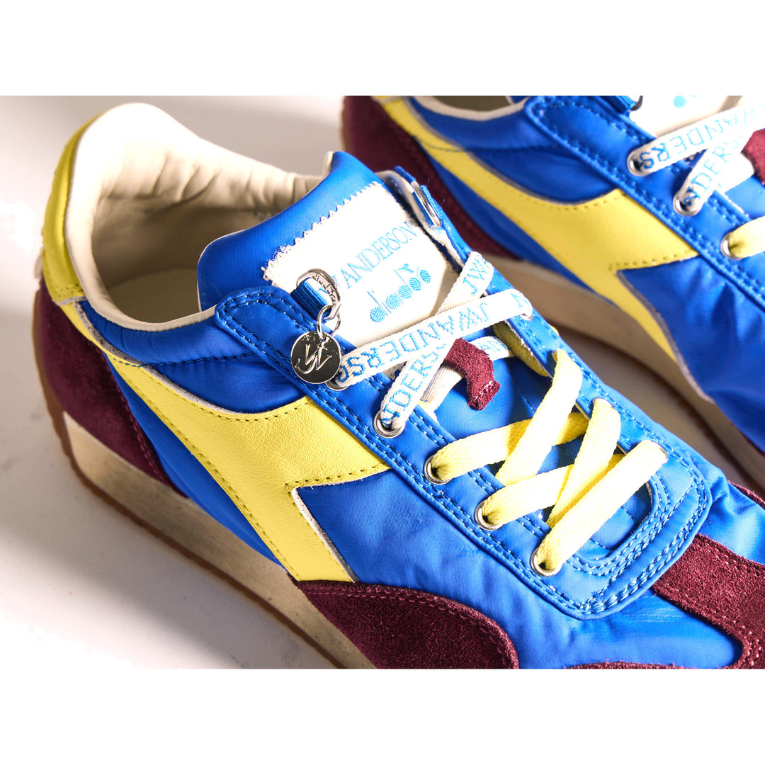 Diadora x JW Anderson retro nylon sneaker in blue with khaki suede overlays, coral laces, and a white Diadora logo stripe, set against a white background - packshot