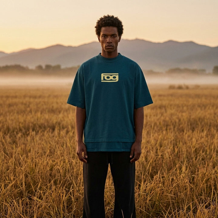 Fear of God ESSENTIALS Panelled Modern Tee in deep teal with a yellow logo graphic at the chest, shown from the front - lifestyle