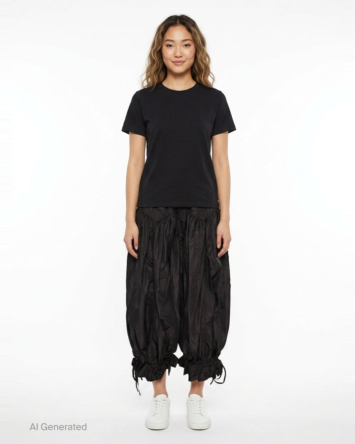 Ganni Flyweight Nylon Balloon Pants in black, featuring a smocked yoke, voluminous gathered body, and ruched tie ankles, displayed flat on a white background - front