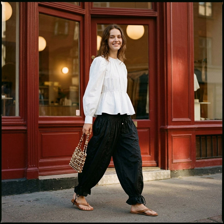 Ganni Flyweight Nylon Balloon Pants in black, featuring a smocked yoke, voluminous gathered body, and ruched tie ankles, displayed flat on a white background - lifestyle
