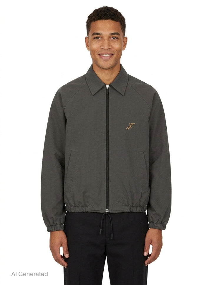 Jacquemus Le Coupe-Vent blouson in slate grey with full-length zip closure, gold script 'J' embroidery on the chest, elasticated cuffs, and drawstring hem - front