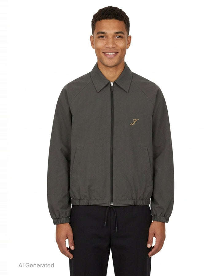 Jacquemus Le Coupe-Vent blouson in slate grey with full-length zip closure, gold script 'J' embroidery on the chest, elasticated cuffs, and drawstring hem - front