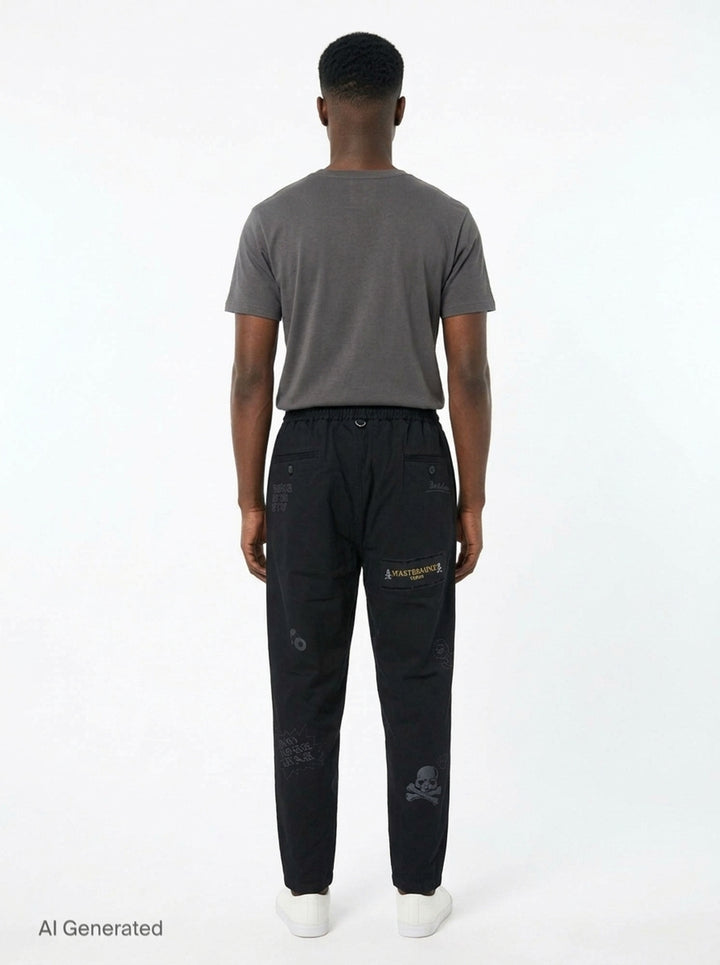 Mastermind Doodle Print Easy Pants in black with all-over graphic prints including skull-and-crossbones, yin-yang symbol, kanji script, and hand-scrawled text, featuring an elasticated drawstring waistband and tapered leg - back