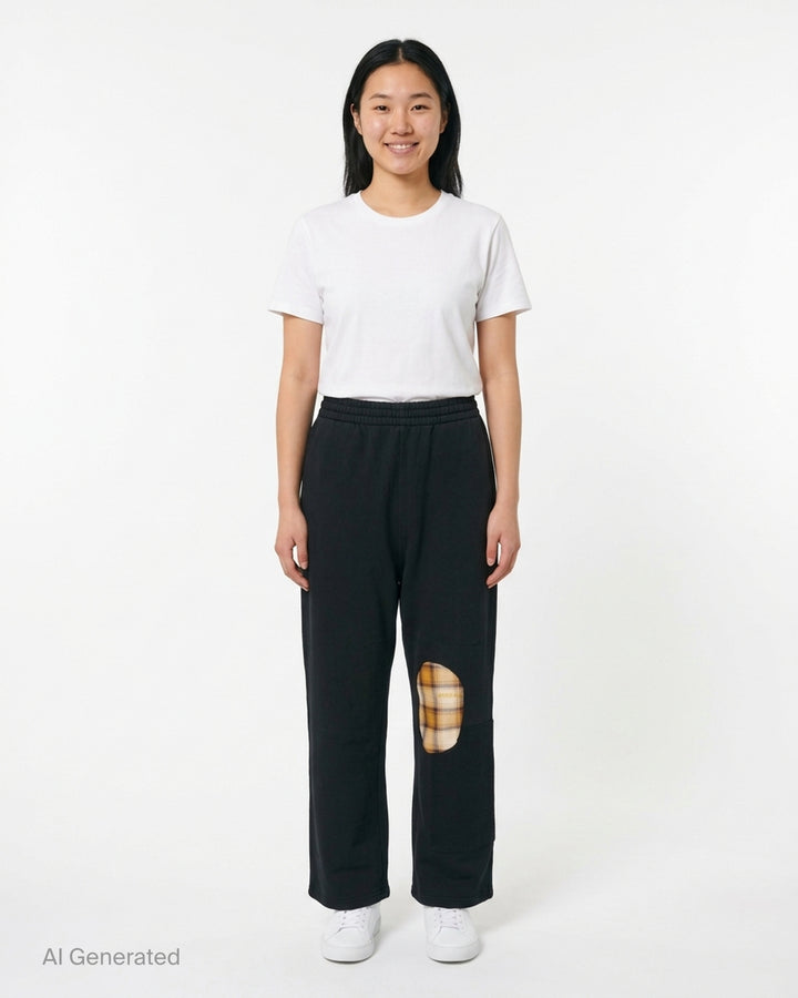 We11done Black Repaired Sweatpants with amber tartan plaid knee patch and embroidered logo, wide-leg relaxed fit, elasticated waistband, front view on white background - front